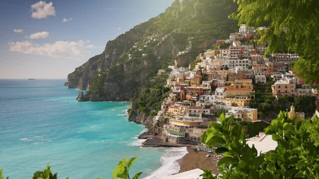 Camera moves between green leaves, overlooking the beach with turquoise water, colorful houses and mountains in Positano village. Beautiful Positano village, Amalfi coast, Italy. Steadycam shot, 4K