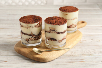 Delicious tiramisu in glasses and spoon on light wooden table