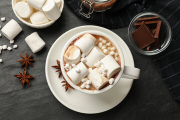 Fototapeta na wymiar Tasty hot chocolate with marshmallows and ingredients on dark textured table, flat lay