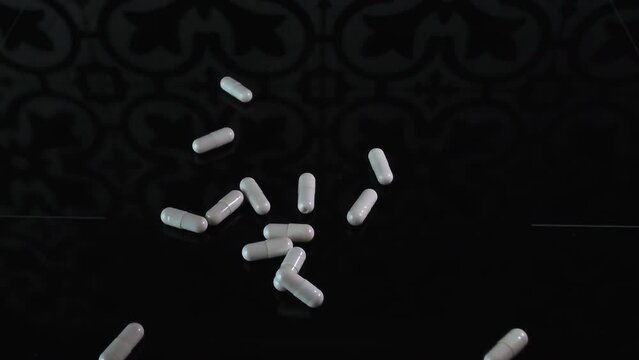 Falling White Capsules on black glass Background, slow motion. Medicine pill capsules falls down, close-up