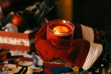 Hands in mittens hold a burning red candle