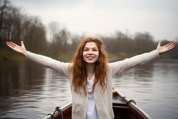 portrait of a young woman standing with her arms raised while on a rowing boat - obrazy, fototapety, plakaty