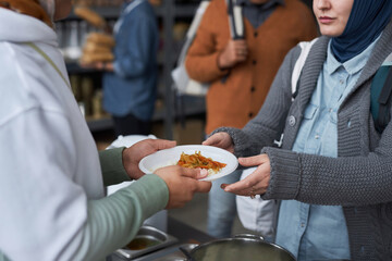Close up of volunteer giving free hot meals to refugees at soup kitchen, focus on hands holding...