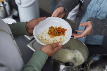 Top view closeup of woman giving hot meals to refugees at soup kitchen, focus on hands holding plate with rice