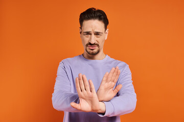 bearded man in purple sweater showing refusal gesture with his hands on orange background - obrazy, fototapety, plakaty
