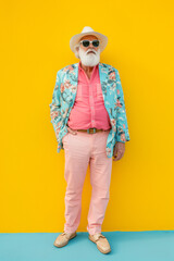Old man dressed modern standing in front of a yellow wall. Colorful.Minimal concept.