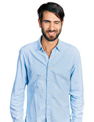 Fototapeta premium Hispanic man with blue eyes wearing business shirt winking looking at the camera with sexy expression, cheerful and happy face.