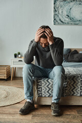 sad bearded man in casual home wear touching head while sitting on bed at home, depression