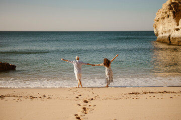 Happy couple facing ocean photographed from their back at the beach, Albufeira, Algarve, Portugal