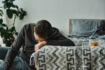 bearded man suffering from pain and leaning on grey blanket on bed in modern bedroom, ache