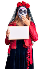 Woman wearing day of the dead costume holding empty white chalkboard covering mouth with hand, shocked and afraid for mistake. surprised expression