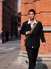 Portrait of handsome Chinese young man with black short hair wearing black blazer posing with modern city building background in sunny winter day, male fashion, cool Asian young man.