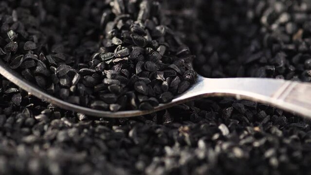 macro black cumin seeds falling on a spoon. slow motion. Asian food seasonings. harvest of black cumin seeds. eating black cumin seeds