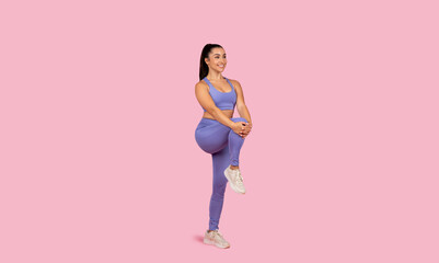 Fototapeta na wymiar Fit woman in sportswear warming up and stretching legs on pink studio background, full length shot, copy space