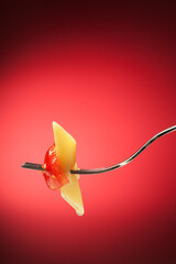 Fork with pasta and tomato on a red background