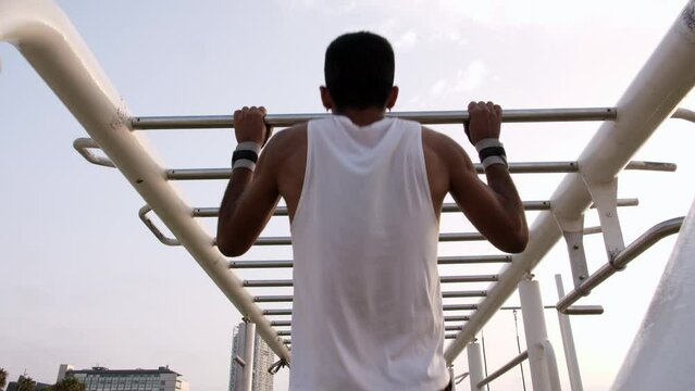 Young latino man doing pull ups in an outdoors calisthenics park by the beach