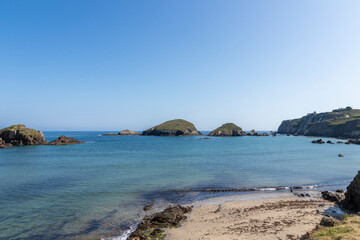 a tranquil beach with clear blue waters, scattered rocky islands, under a bright sky, creating a picturesque landscape