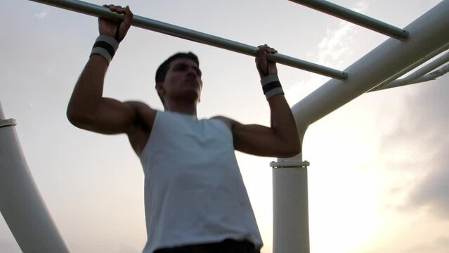 Young latino man doing pull ups in an outdoors calisthenics park during sunrise