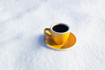 Obraz na płótnie Canvas Winter background. Yellow cup with hot coffee or tea stand on the snow outdoor at sunny day with cold weather outdoors.