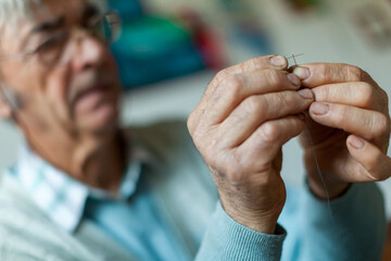 Old Man With Glasses Trying To Put Thread trough Hole of Sewing Needle