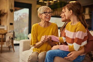 Focus on the grandma, smiling at her grandchild while the little girl is sitting on her moms lap,...
