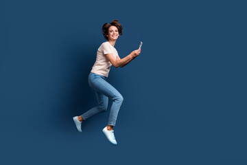 Fototapeta na wymiar Full length photo of lovely young lady running hold telephone hurry shopping dressed white garment isolated on dark blue color background
