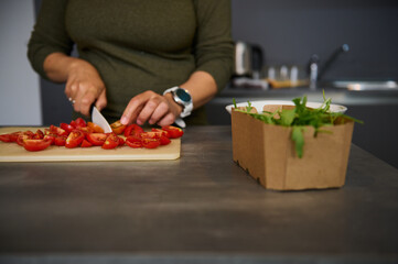 Close-up woman housewife cutting tomatoes, preparing fresh salad, standing at kitchen table
