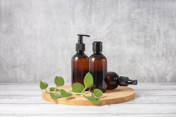cosmetic bottles on a wooden board and a sprig of mint on a gray background