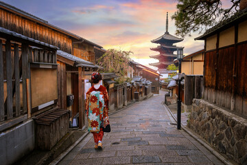 Fototapeta premium Scenic cityscape of Yasaka pagoda sunset in Kyoto with a young Japanese woman in a traditional Kimono dress during full bloom cherry blossom in spring
