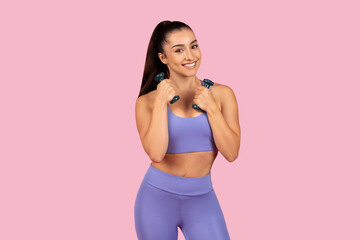 Fototapeta na wymiar Smiling caucasian lady in sportswear doing exercises with hand dumbbells, enjoying workout on pink background