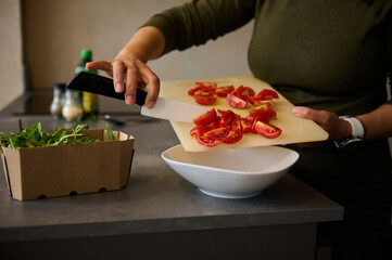 Chef hands with knife, cutting red tomatoes for salad. Fresh vegetables, arugula leaves and olive oil on the table