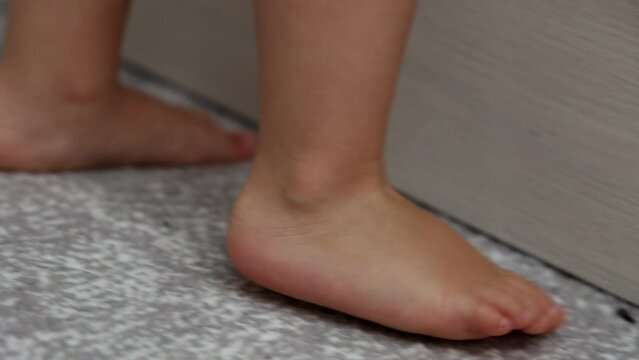 baby boy toddler feet on floor. kid child is jumping, playing next to bed.