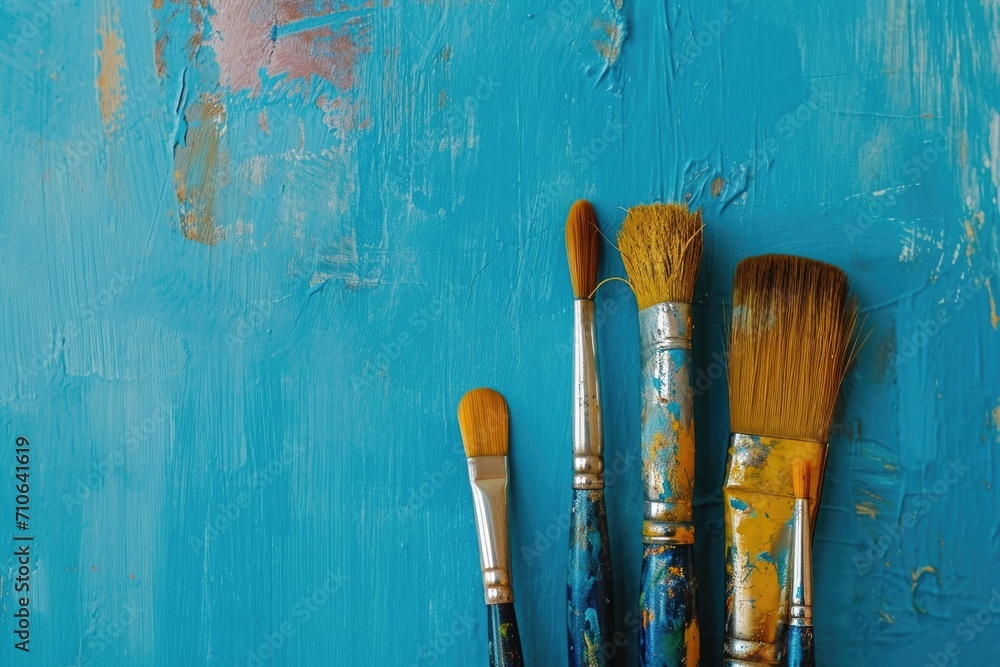 Aufkleber Three paint brushes are sitting next to each other on a blue wall. This image can be used for various art-related concepts and design projects