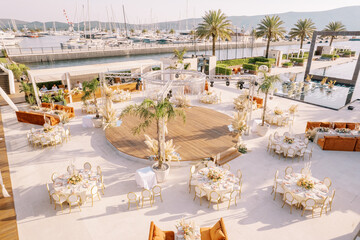 Covered tables stand around a circular stage in front of the pool on a sun terrace by the sea