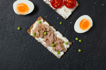 Ingredients for sandwich with boiled egg, cherry tomatoes, canned tuna, garlic and spices over black grunge background. High quality photo