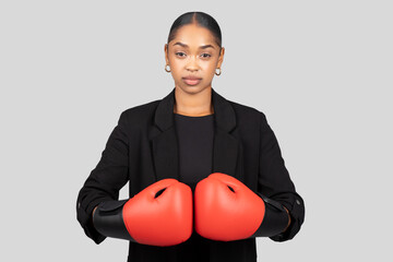 Determined businesswoman in a black blazer with boxing gloves on, ready to face challenges