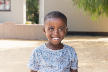 happy african kid in the village, standing in the yard, home in the background, late afternoon