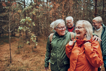 Group of senior friends laughing and walking together in autumn forest