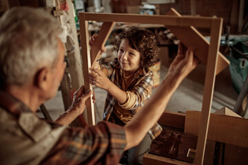 Obraz na płótnie Canvas Grandfather and grandson enjoying woodworking in a home workshop