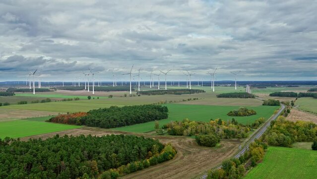 Drone approach to a wind farm during cloudy weather  between forests and fields