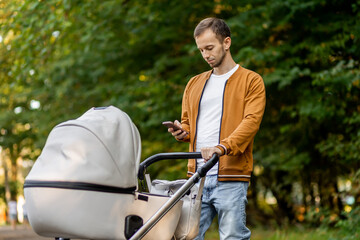 father pushing a baby stroller and typing on a mobile phone in park. Waterproof and windproof...