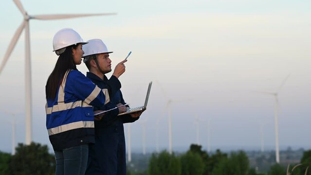 Two engineers working and holding the report at wind turbine farm Power Generator Station on mountain,Thailand people,Technician man and woman discuss about work