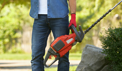 Unrecognizable muscular man in jeans standing with modern electric hedge trimmer outdoors. Crop...