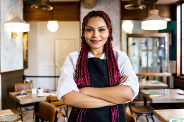 A dark-skinned woman in a waitress uniform poses happily with her arms crossed while looking at the...