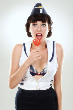 Portrait, surprise and sailor woman with lollipop in studio isolated on a white background. Candy, wow and shocked air hostess with sugar food, heart sweets or travel dessert for vintage pin up girl