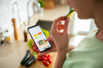 Woman using a meal planning app on smartphone in kitchen