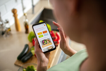Woman using a meal planning app on smartphone in kitchen