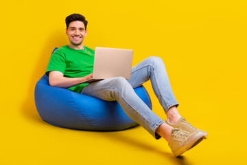 Full length photo of intelligent smart man dressed green t-shirt sit on pouf with laptop write...