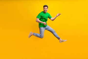 Fototapeta na wymiar Full size photo of good mood optimistic guy wear stylish t-shirt jumping play on imaginry guitar isolated on yellow color background