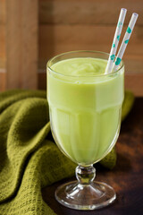 avocado smoothie, healthy and refreshing, in a glass bowl, with blue biodegradable straws, composition and production with a green cloth and wood in the background, summer body, vertical photography